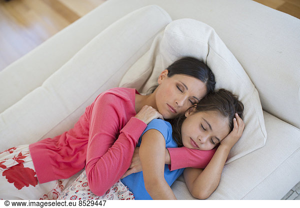 Mother and daughter napping on sofa in living room