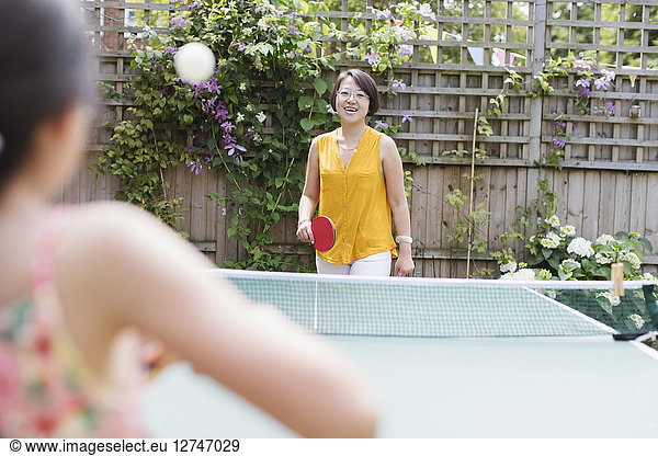 Mother and daughter playing table tennis in sunny backyard