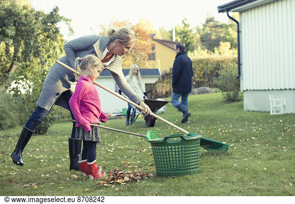 Mother and daughter raking autumn leaves at yard