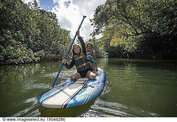 Mother and daughter relaxing while paddling paddle board Waimea river