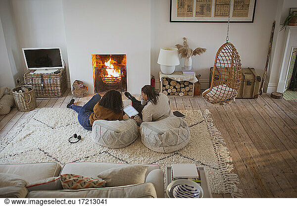 Mother and daughter relaxing with digital tablet by cozy fireplace