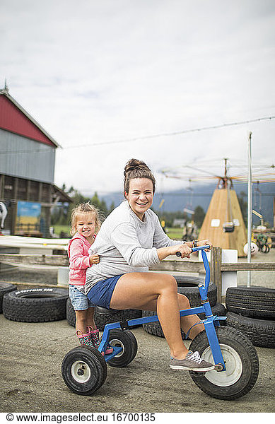Mother and daughter riding on tricycle on racetrack.