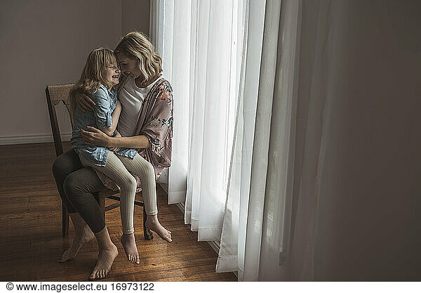 Mother and daughter sitting close together near window in studio