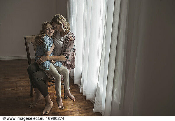 Mother and daughter sitting close together near window in studio