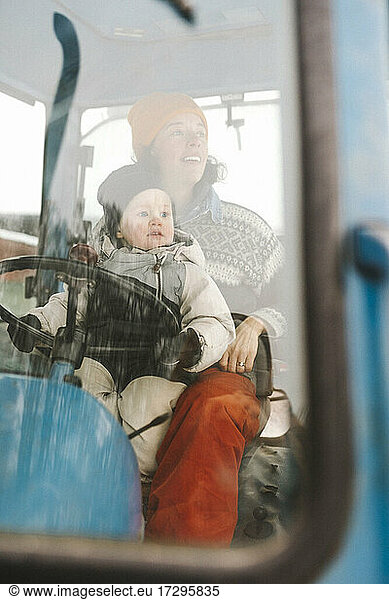 Mother and daughter sitting in tractor seen through windshield