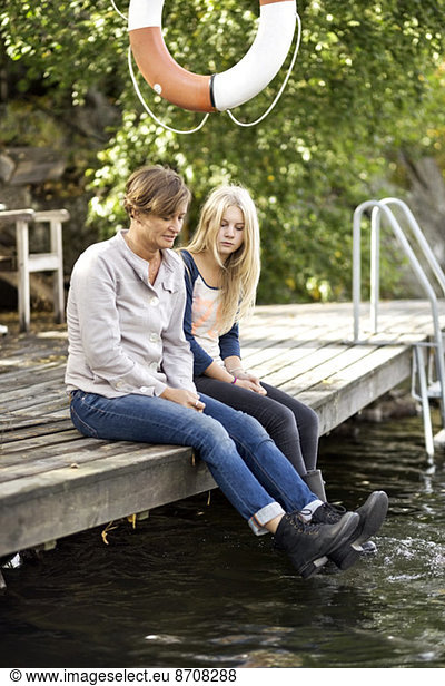 Mother and daughter sitting on pier
