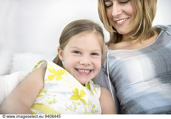 Mother and daughter sitting on sofa  smiling