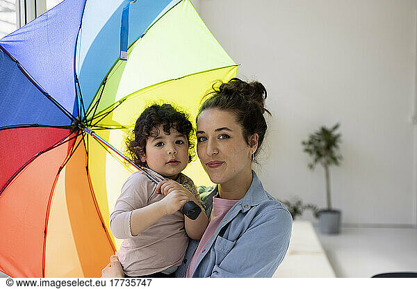 Mother and daughter standing at home holding umbrella