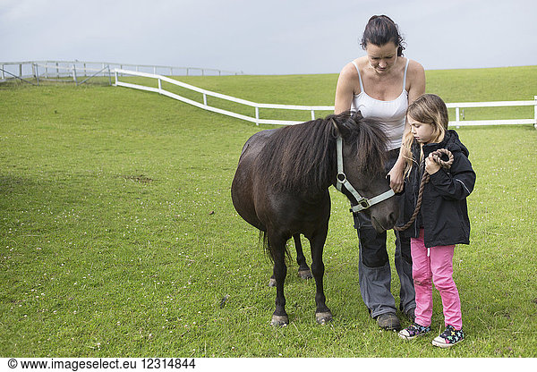 Mother and daughter (4-5) standing with pony