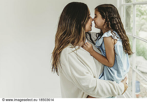 Mother and daughter touching noses in natural light studio