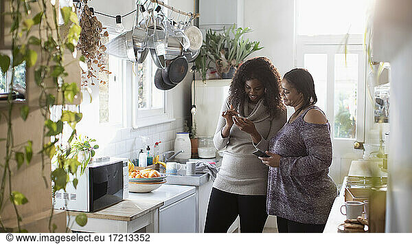 Mother and daughter using smart phones in kitchen