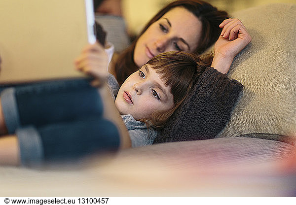 Mother and daughter using tablet computer while lying on sofa at home
