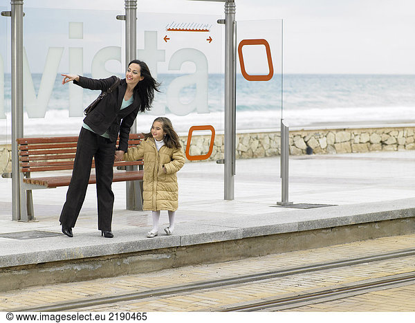 Mother and daughter (6-8) waiting at tram stop on coast