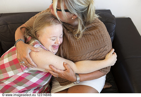 Mother and daughter with down syndrome embracing on sofa