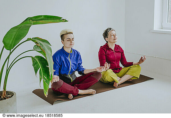 Mother and daughter with eyes closed meditating at fitness studio