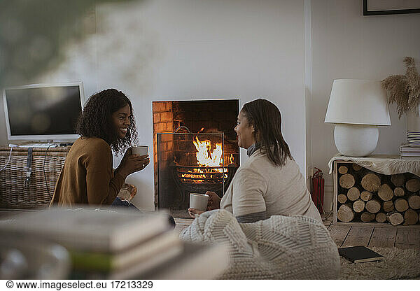 Mother and daughter with tea talking at fireplace in cozy living room