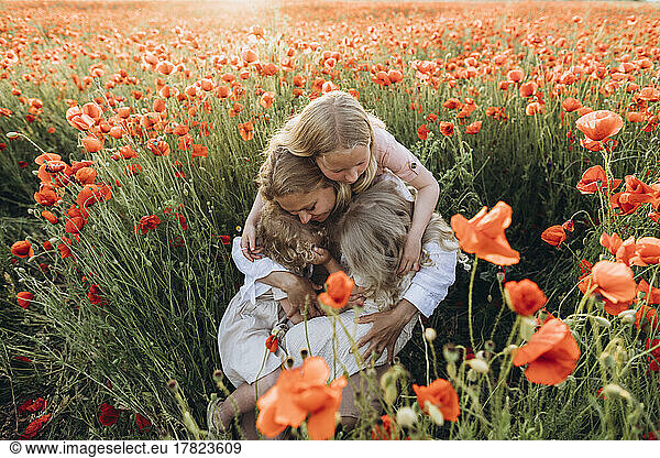 Mother and daughters embracing each other in poppy field