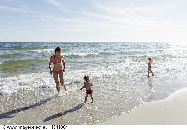 Mother and daughters enjoying on beach against sky during sunny day