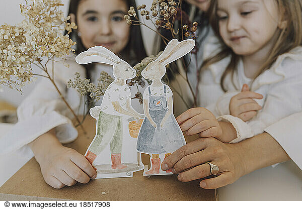 Mother and daughters holding paper Easter bunnies at home