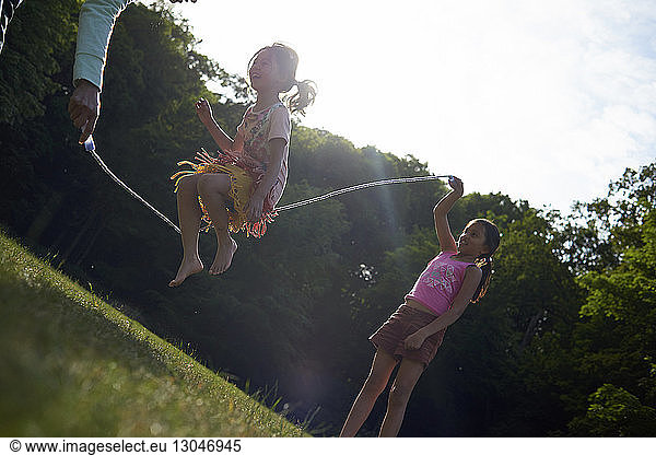 Mother and daughters playing with jump rope at park during summer