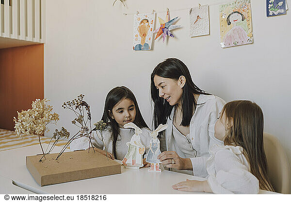 Mother and daughters playing with paper Easter bunnies at home