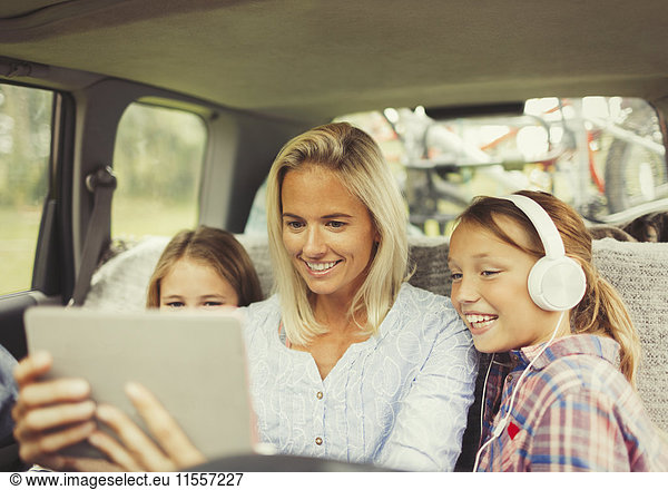 Mother and daughters watching video on digital tablet in back seat of car