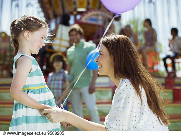 Mother and girl with balloon looking at each other in amusement park