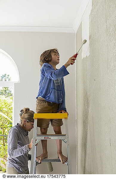 mother and her 8 year old boy using paint rollers to paint wall