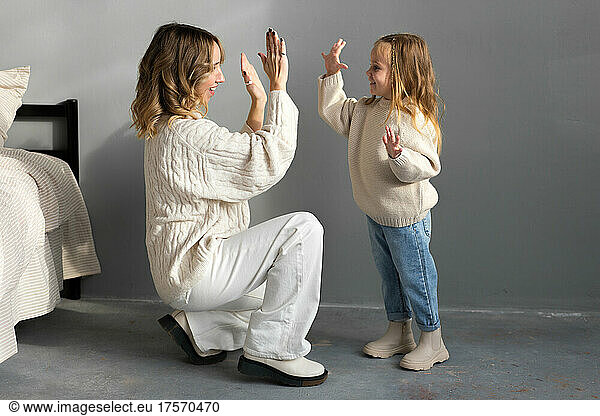 Mother and little daughter in cozy family outfits claping in han