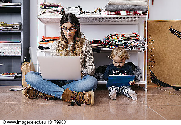 Mother and little daughter sitting on the floor at home using laptop and tablet