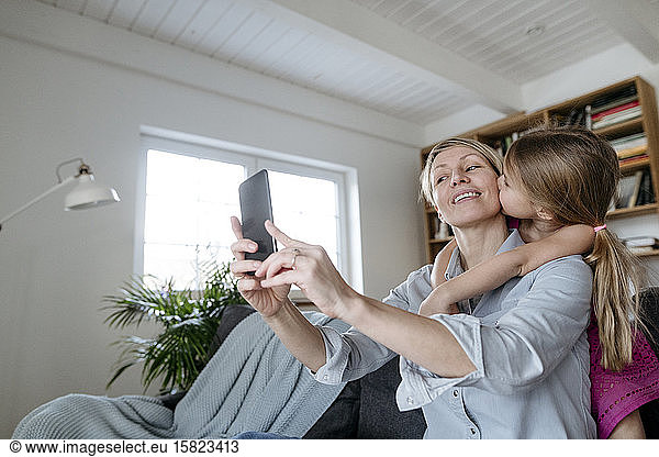 Mother and little daughter taking selfie with smartphone at home