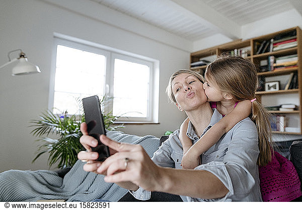 Mother and little daughter taking selfie with smartphone at home