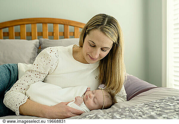 Mother and newborn baby lying on bed; mom looking down at baby smiling