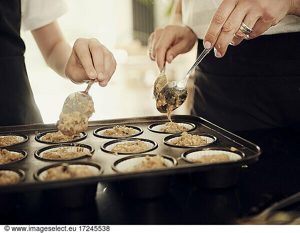 Mother and son filling muffin tray with batter in kitchen