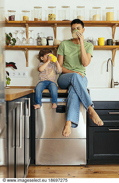 Mother and son having drinks sitting on kitchen counter at home