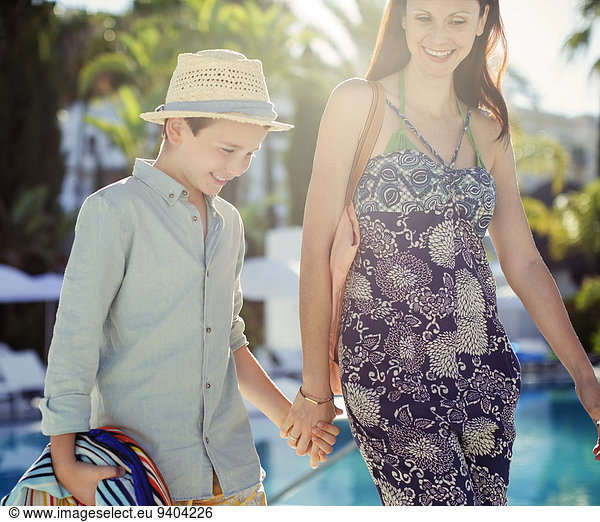 Mother and son holding hands by swimming pool