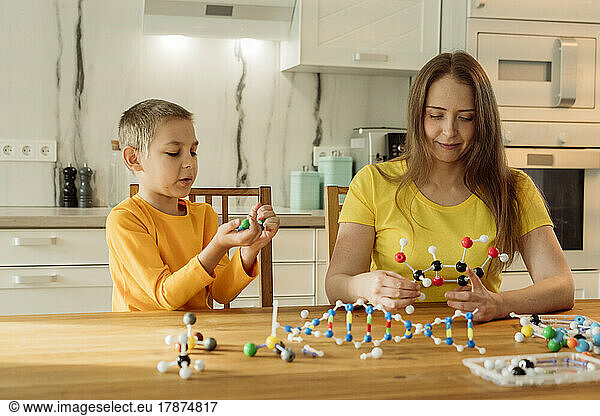 Mother and son holding molecules on table at home