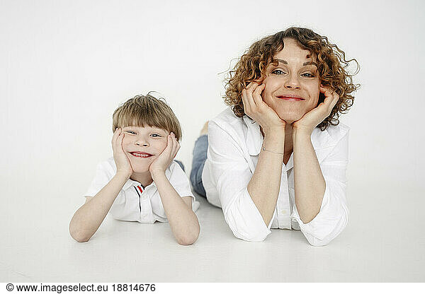 Mother and son leaning on elbows lying in front of white backdrop
