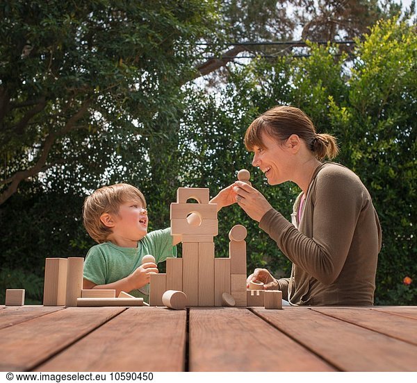 Mother and son playing with wooden building blocks in garden