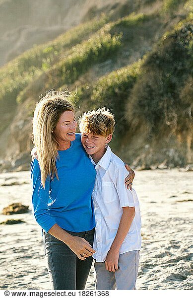 Mother And Tween Son Embrace And Laugh At The Beach