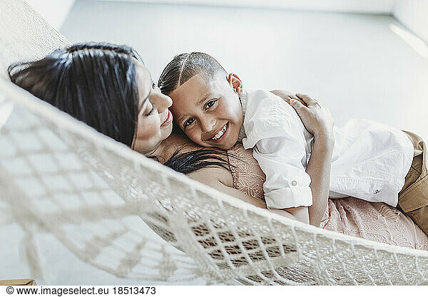 Mother and young son cuddling while laying in hammock in studio
