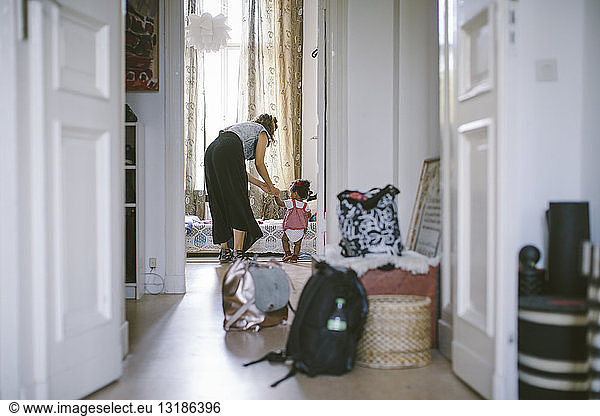 Mother assisting daughter in walking seen through doorway at home