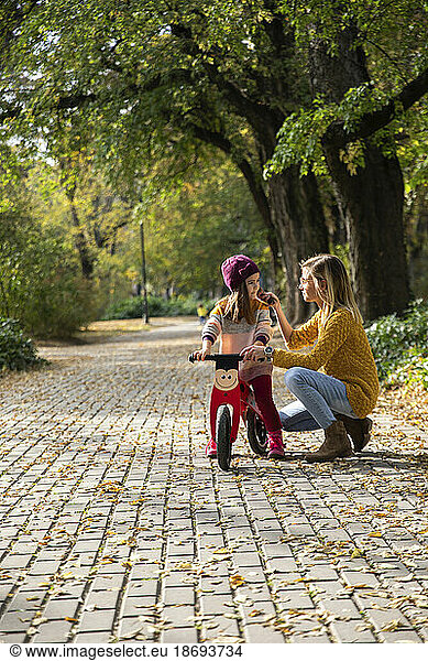 Mother assisting daughter sitting on bicycle at park