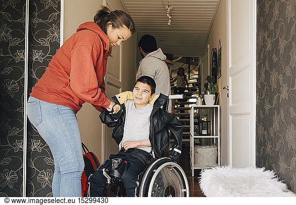 Mother assisting disabled son in wearing jacket at home