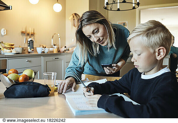 Mother assisting son while doing homework at home