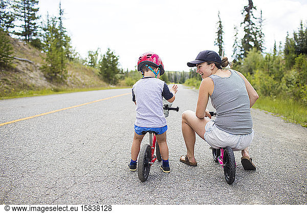 Mother biking and laughing with son on a small balance bike.