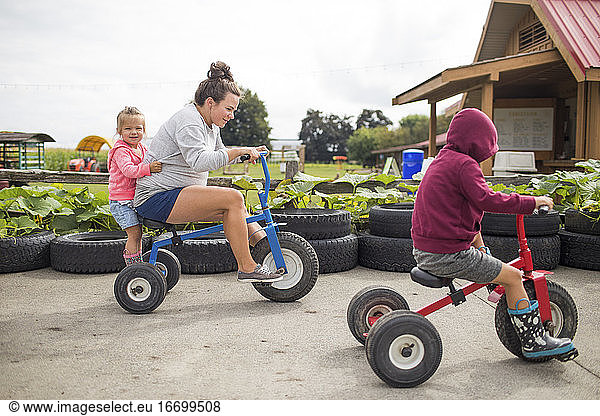 Mother biking on tricycles with her two kids outdoors.