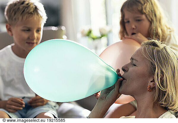 Mother blowing balloon with children at home
