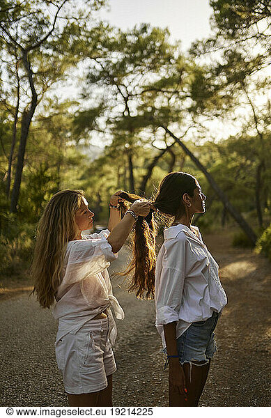 Mother braiding daughter's hair standing on road in forest