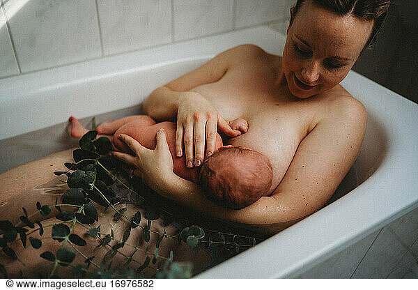 Mother breastfeeding newborn baby in bath tub after birth skin to skin